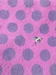 A purple quilt with a bird on it.