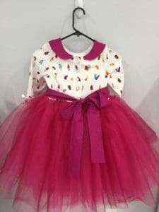 A pink dress with butterflies on it hanging from a wall.