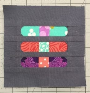 A quilt block with three different colored bandaids on it.