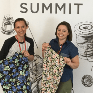 Two women holding up fabric samples in front of a wall.