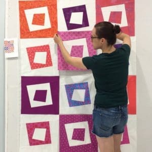 A woman is standing in front of a wall with squares on it.