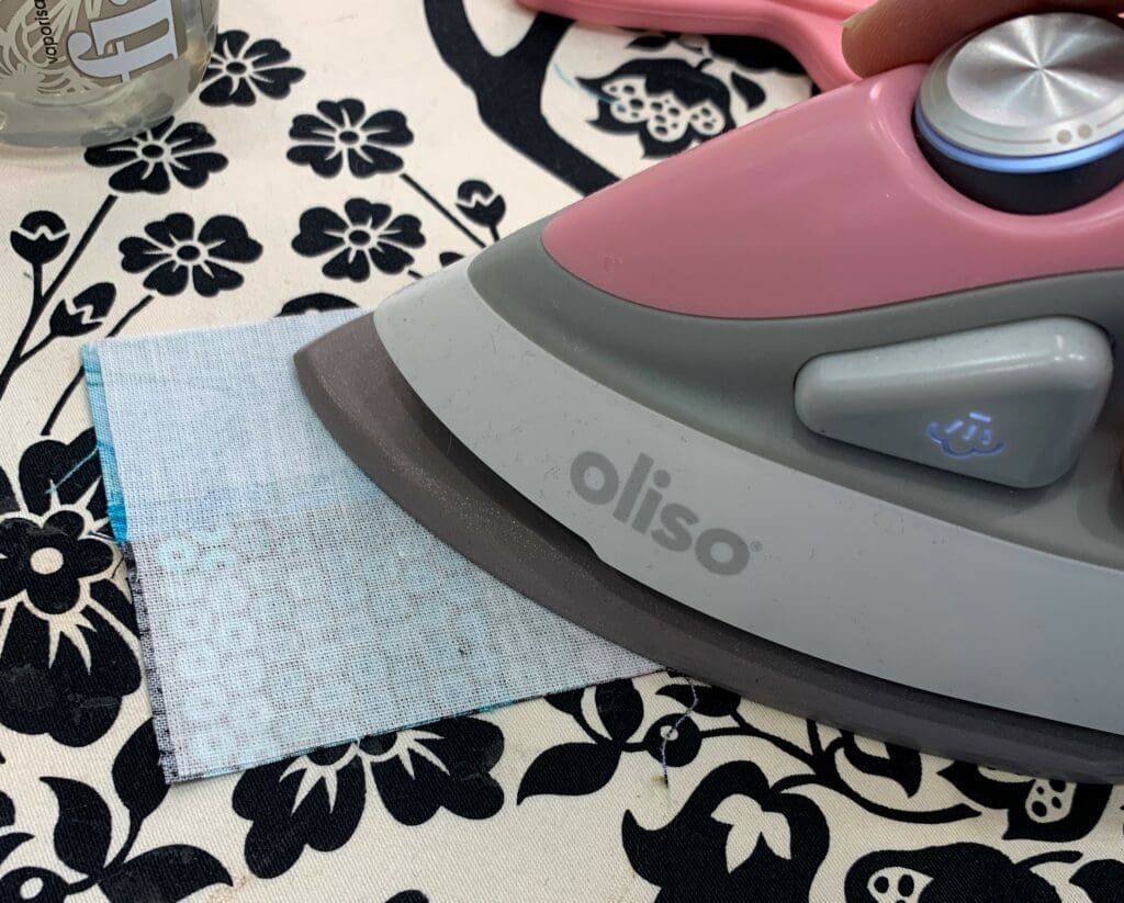A pink iron sitting on top of a floral patterned table.