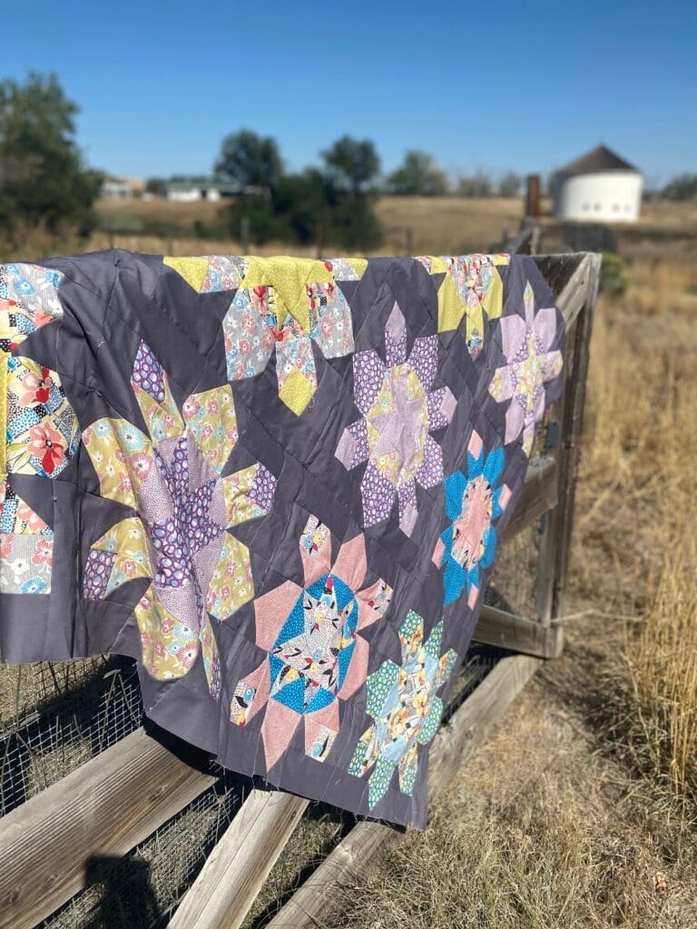 A quilt hanging on the side of a wooden fence.