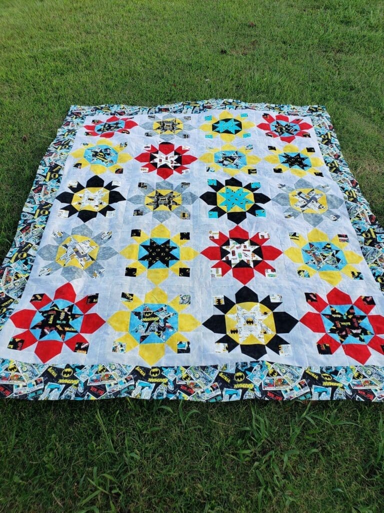 A quilt is displayed on the grass.