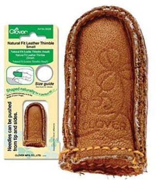 A brown leather thimble with a stitch on it.