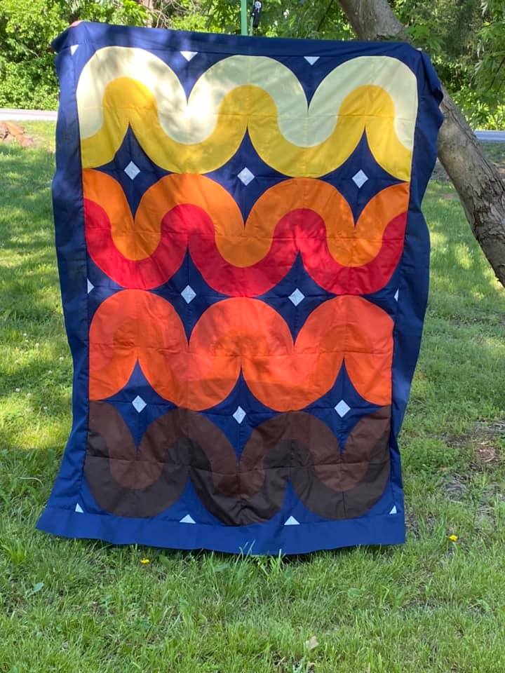 A colorful quilt sitting on top of grass.