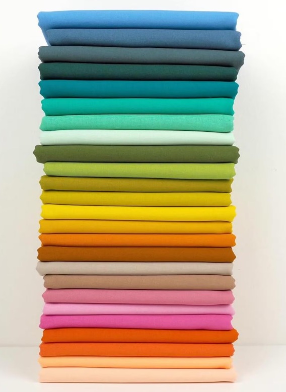 Neatly stacked colorful fabric pieces arranged in a gradient from green to pink.