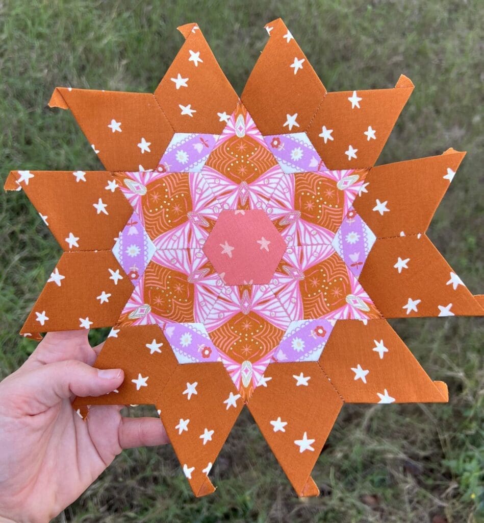 Hand holding a colorful, star-shaped mandala on grass.
